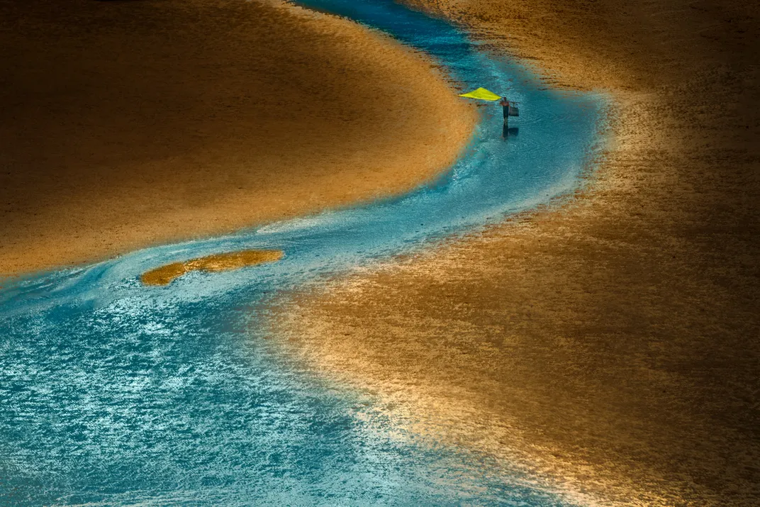 A beach at sunset with a fisherman wading through the body of water