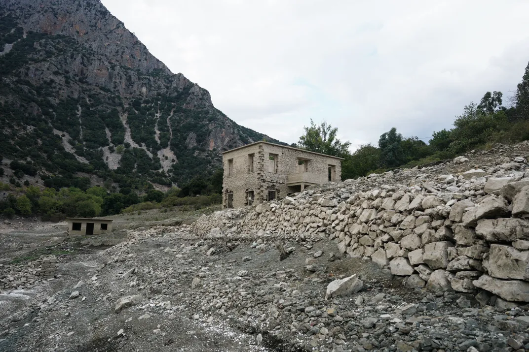 an abandoned house stands on a rocky bank of the lake